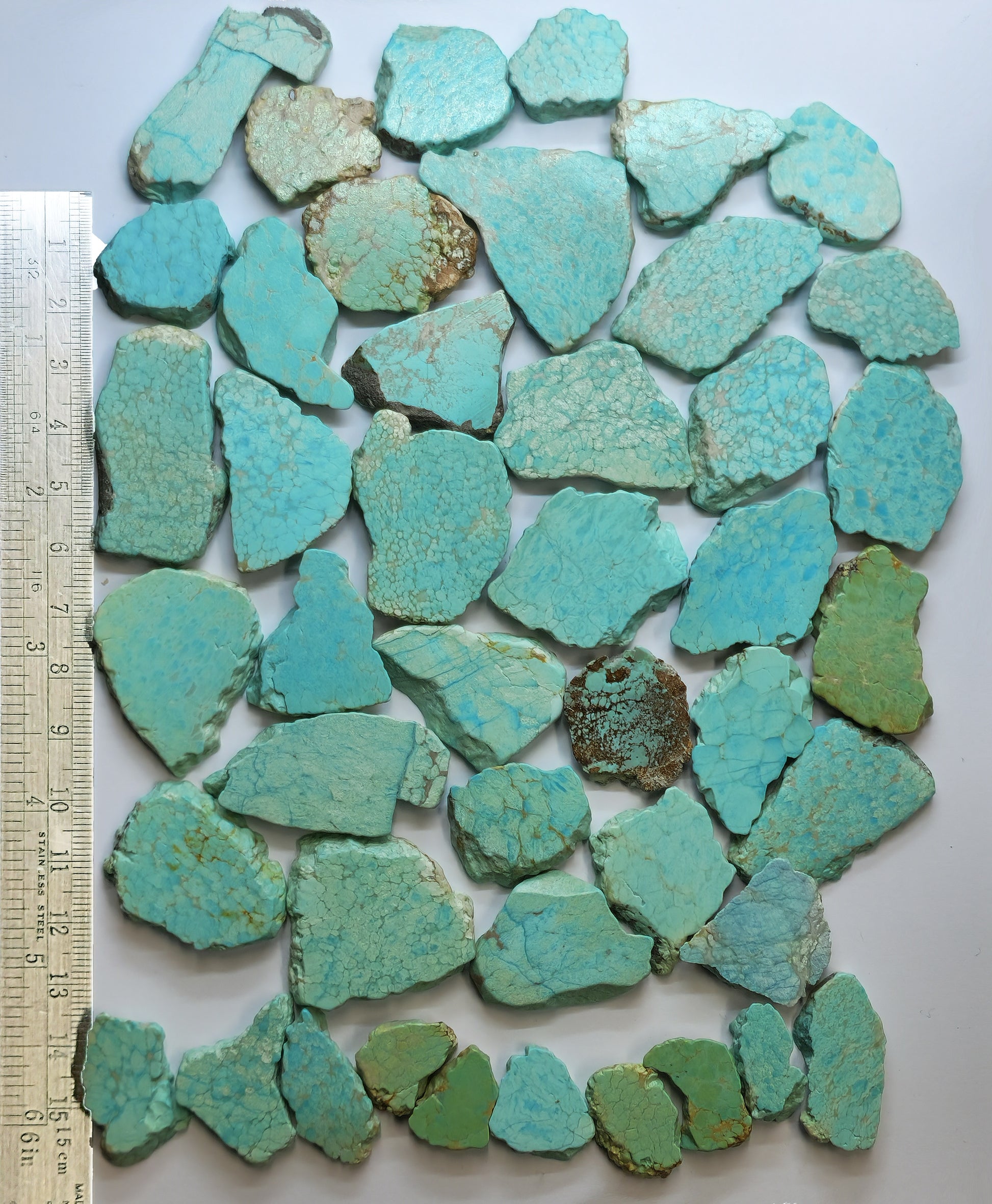Turquoise stone fragments with a ruler for scale on a white background